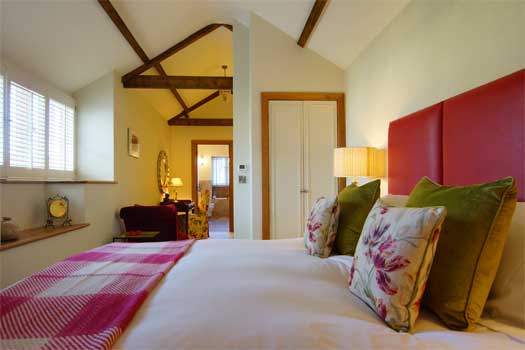 Elegant super-king bedroom at The Dairy with vaulted ceiling, exposed timber beams and country-style furnishings