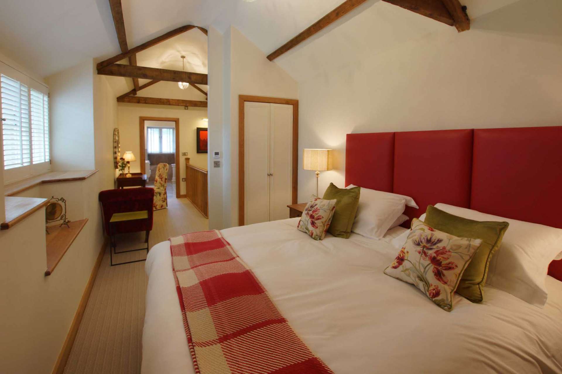 Super-king bedroom at The Dairy showing the vaulted ceiling, red upholstered headboard and view through to the landing